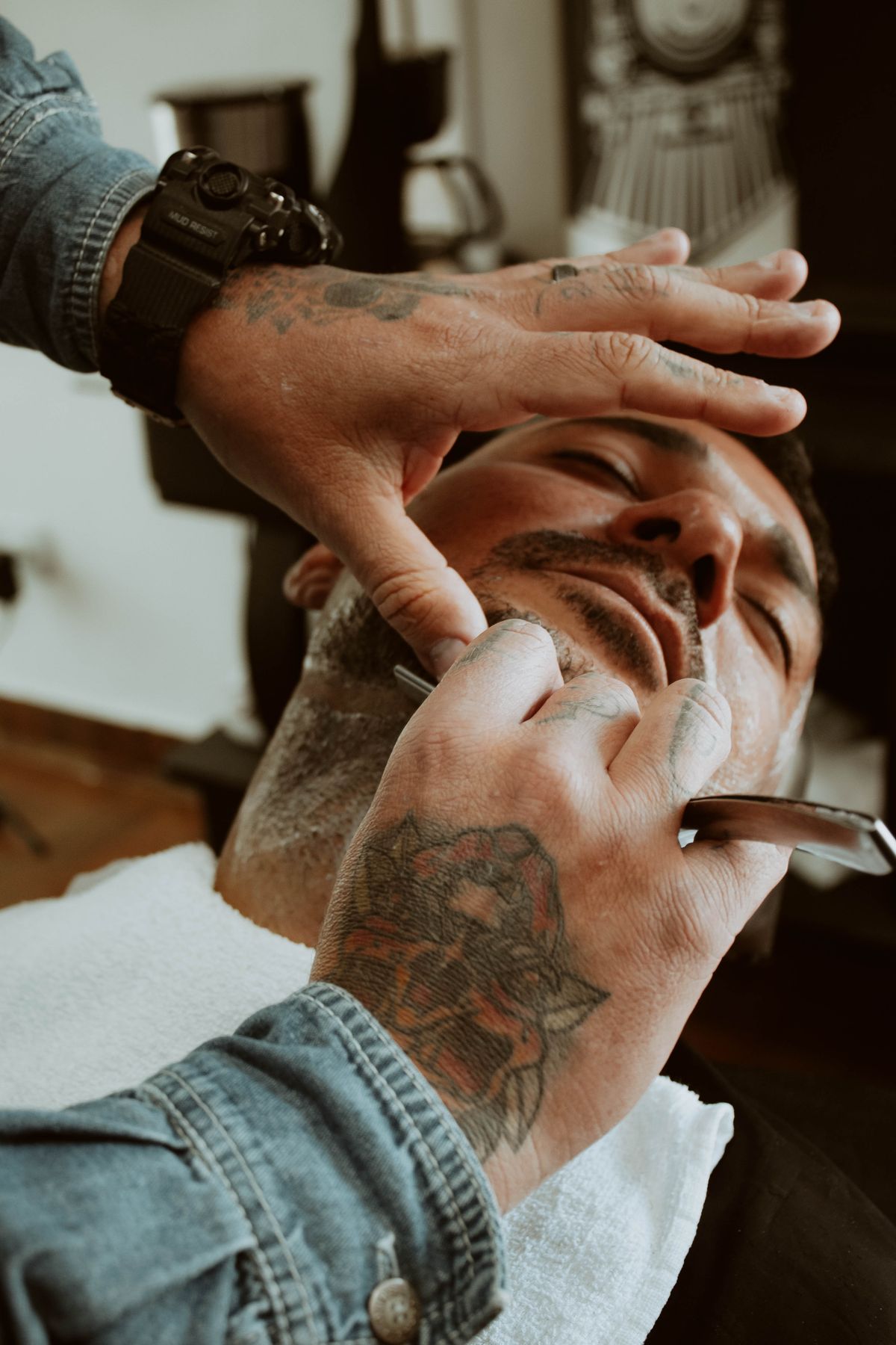 Barbeiro fazendo a barba de um cliente com navalha